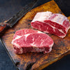 Two raw steaks on a wooden cutting board with a cleaver.